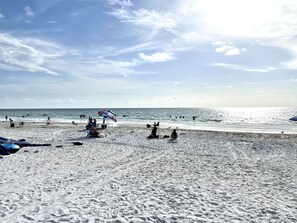 A beach with people swimming and sunbathing, a colorful umbrella, and footprints in the sand. - Cute, spacious 2 BR 2 Full BA condo minutes from the beaches (Largo)