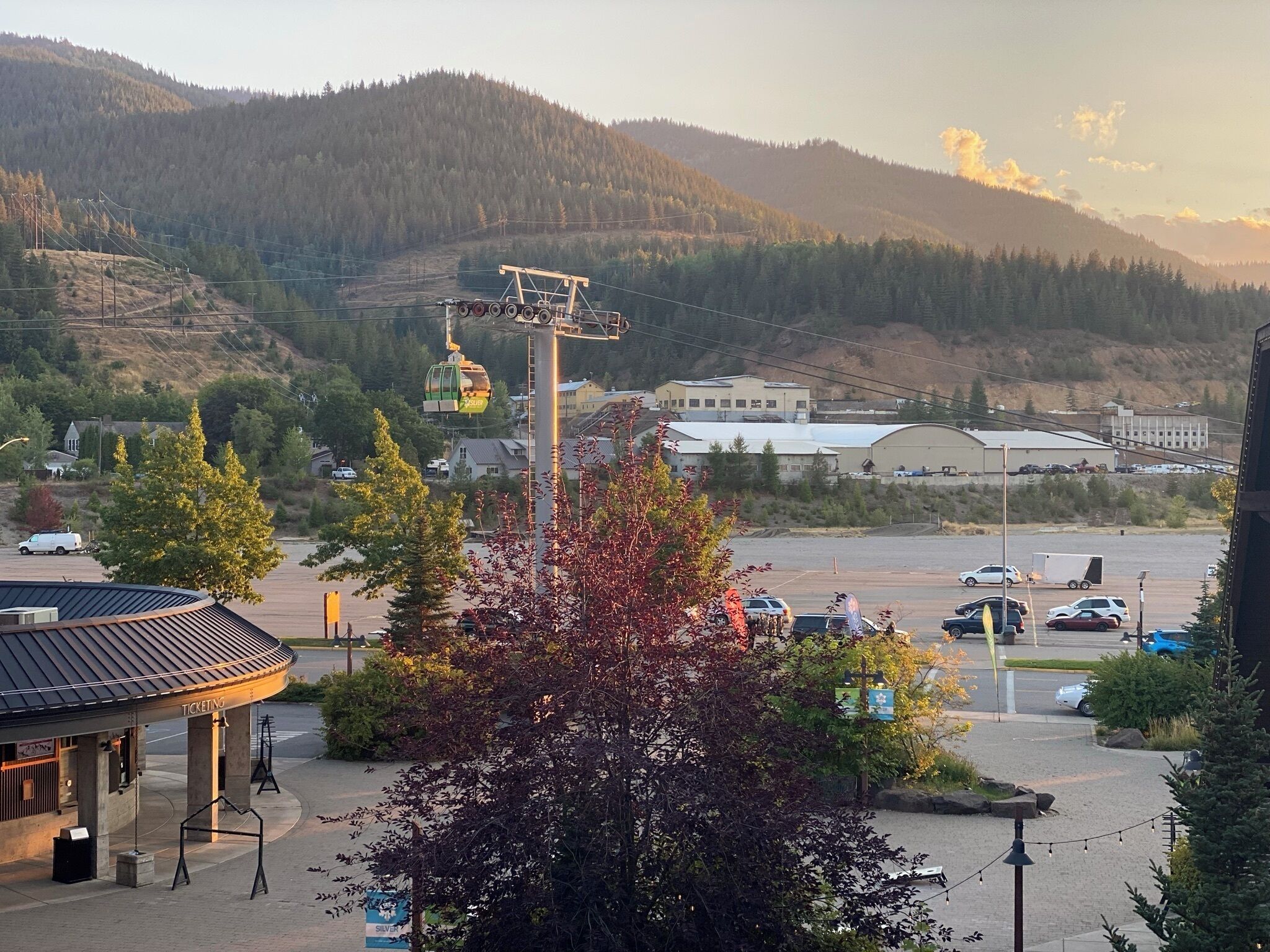A parking area with a ticketing booth, a ski lift, and a mountainous backdrop.