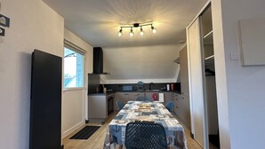 A compact kitchen with a dining area, featuring a black refrigerator, a built-in oven, a stove, and a ceiling light fixture. - Apartment T3 in Carnac plage (Carnac)