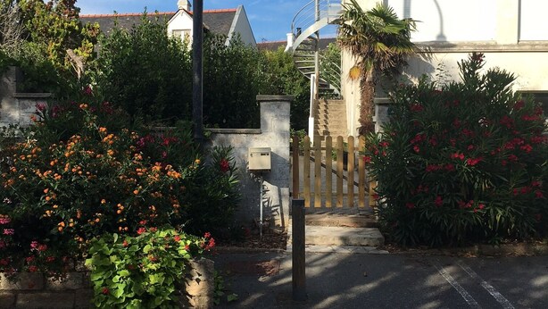 A residential street with a crosswalk, a metal bollard, and a house with a visible staircase leading to a second-floor window. - Apartment T3 in Carnac plage (Carnac)
