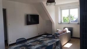 A dining area with a table covered in a patterned tablecloth, a television mounted on the wall, and a sofa with cushions. - Apartment T3 in Carnac plage (Carnac)