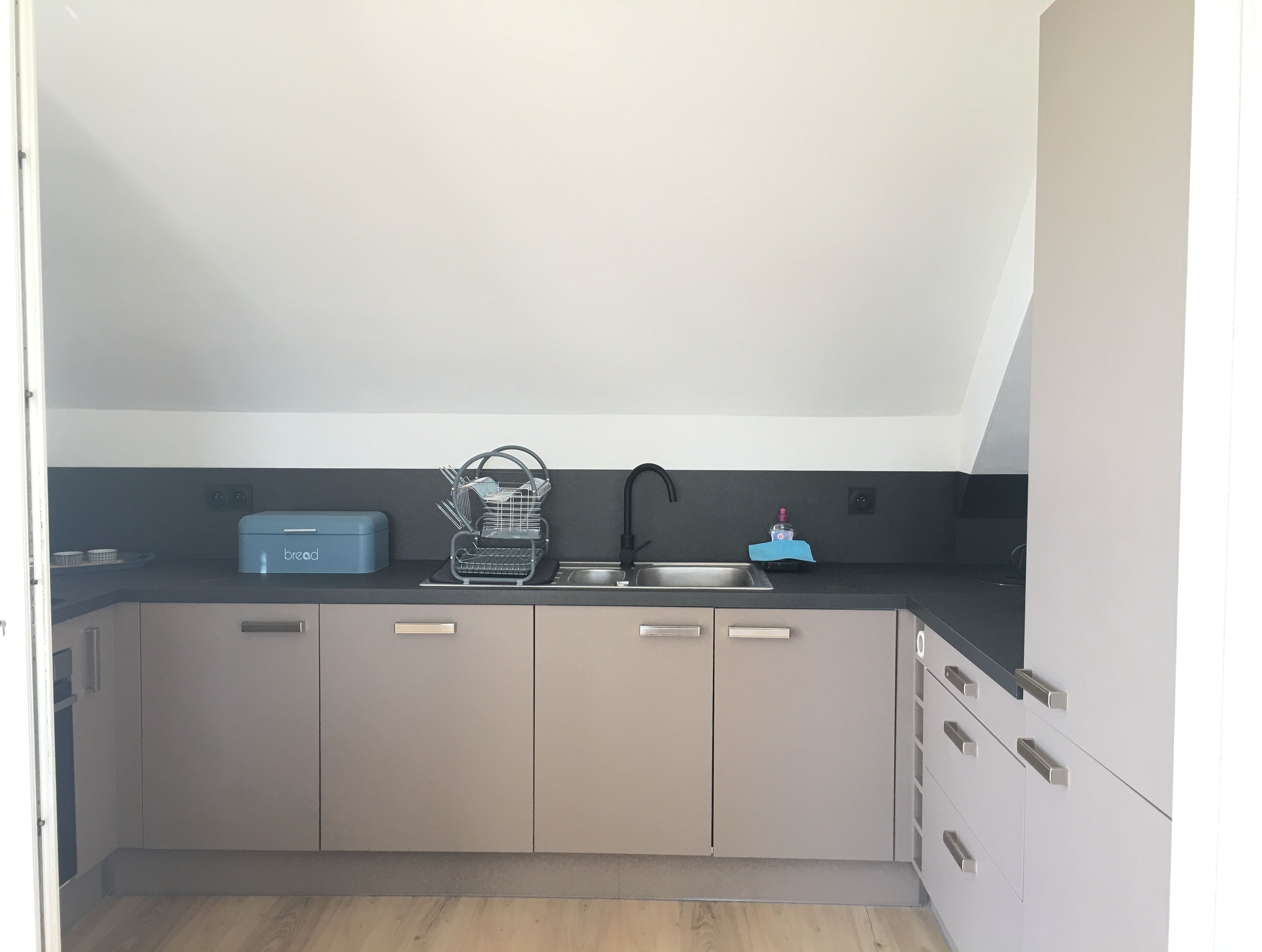 A modern kitchen with a black countertop, a built-in sink, and a bread box.