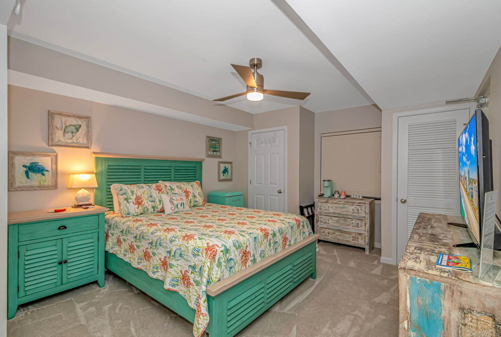 A bedroom with a bed, a nightstand, a dresser, a ceiling fan, and a television.