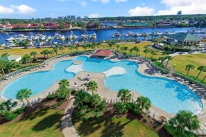 A large, irregularly shaped swimming pool with a surrounding deck and palm trees, set against a backdrop of a marina with boats and buildings. - Intercostal Waterway Hotel Style Room -- 5 min from the beach! (North Myrtle Beach)