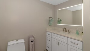 A bathroom with a white toilet, a sink with a mirror, and a towel rack. - Intercostal Waterway Hotel Style Room -- 5 min from the beach! (North Myrtle Beach)