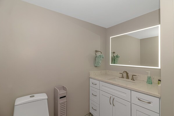 A bathroom with a white toilet, a sink with a mirror, and a towel rack. - Intercostal Waterway Hotel Style Room -- 5 min from the beach! (North Myrtle Beach)