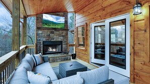 A wooden deck with a stone fireplace, outdoor seating, and large sliding glass doors.