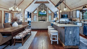 A spacious kitchen with a central island, wooden beams, and a stone fireplace.