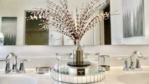 A bathroom with a round mirror, two sinks, and a decorative vase with branches.