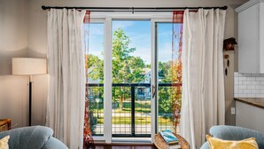 Ein Wohnzimmer mit einer großen Schiebeglasdoor zum Balkon, einem Sofa, einer Lampe und einem kleinen Tisch mit Büchern.