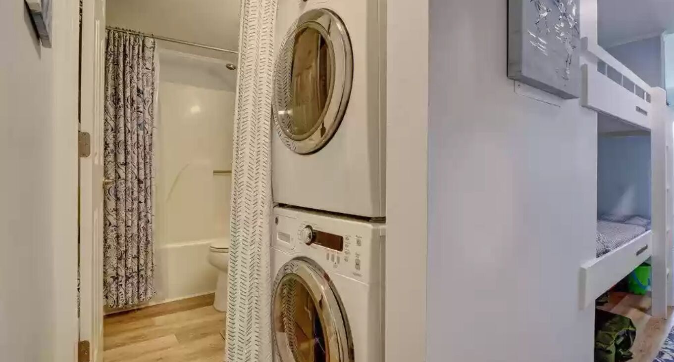 Un lavadero con dos lavadoras apiladas, una cortina de ducha y un inodoro.