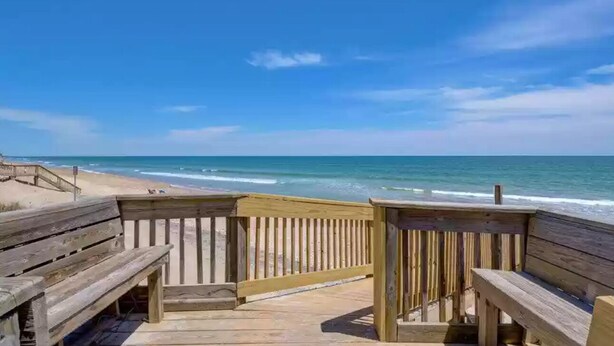 A wooden boardwalk leading to a beach with a clear view of the ocean.