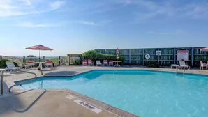 A swimming pool with lounge chairs and umbrellas, surrounded by a fence and a building with signage.