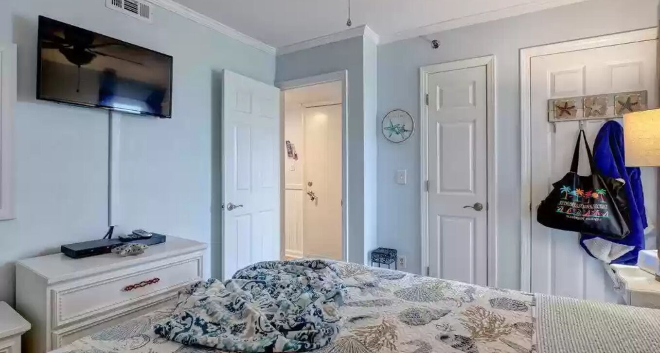 Une chambre à coucher comprenant un lit, une commode, un téléviseur et une porte donnant accès à une salle de bain.