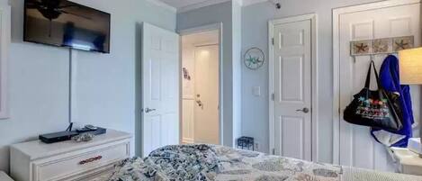 Une chambre à coucher comprenant un lit, une commode, un téléviseur et une porte donnant accès à une salle de bain.