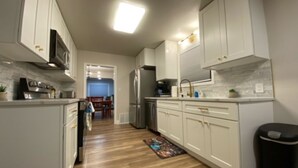 A modern kitchen with white cabinets, stainless steel appliances, and a wooden floor.
