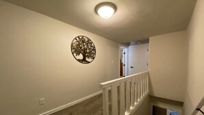 A hallway with a white railing, a wall-mounted tree decoration, and a carpeted floor.