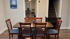 A dining area with a wooden table and chairs, a chandelier, and a painting on the wall.