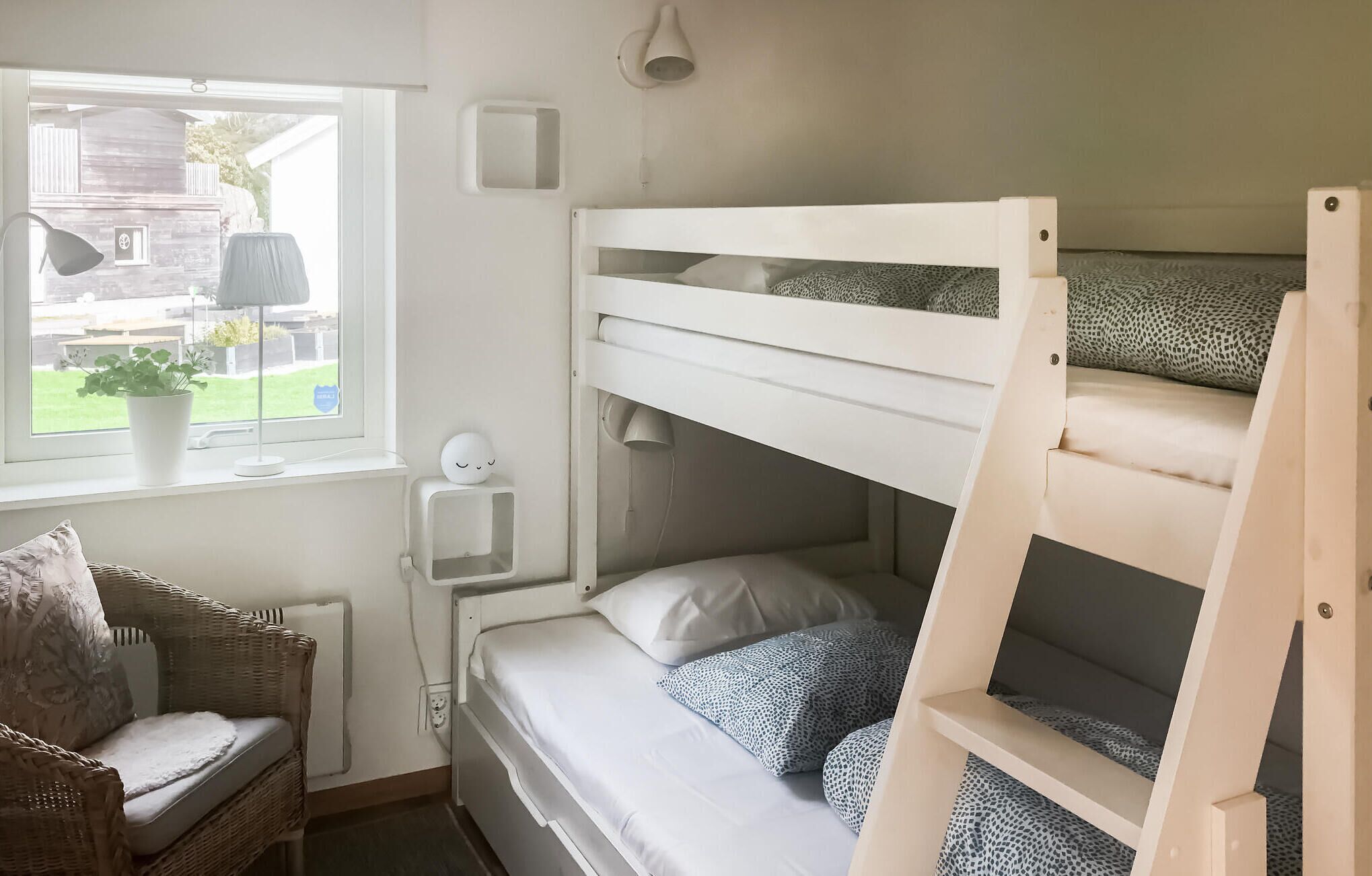 Une chambre avec un lit superposé, une fenêtre, une table de chevet, une lampe et une chaise en osier.