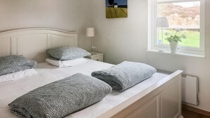 Un dormitorio con una cama individual, una mesita de noche, una lámpara, una ventana con vistas al exterior y un cuadro en la pared.