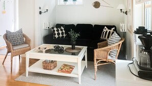 Una sala de estar moderna con un sofá blanco, dos sillones de mimbre, una mesita de centro y una cocina con estufa.