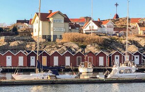 Ein Yachthafen mit anlegenden Booten, eine Reihe roter Holzhäuser und Häuser an einem Hügel.