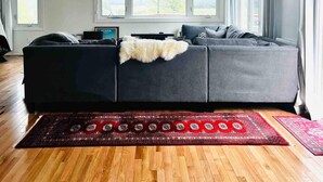 A modern living room with a sectional sofa, a projector ceiling, large windows, and a red patterned rug.