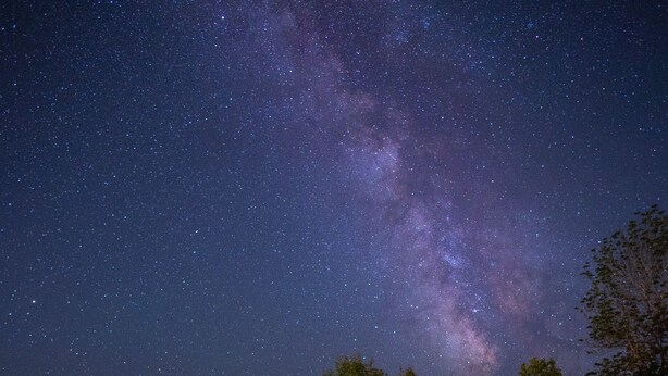 A deck with two chairs and a small table under a night sky with visible stars and the Milky Way.