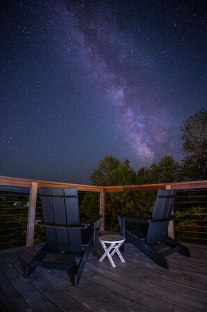 A deck with two chairs and a small table under a night sky with visible stars and the Milky Way.