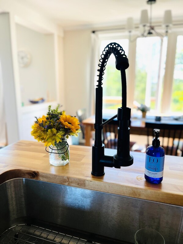 A kitchen sink with a modern faucet, a vase of yellow flowers, and a bottle of hand soap on the counter.
