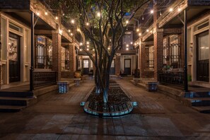 Un patio con un árbol, edificios de ladrillo y luces colgantes.