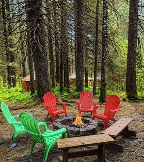 Uma fogueira cercada por cadeiras Adirondack vermelhas e verdes, com uma mesa de madeira na frente.