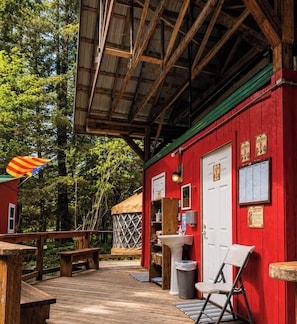 A wooden deck with a red building, a white door, a sink, and a bench. - Nauti Otter Inn and Yurt Village (Seward)