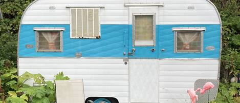 Une caravane ancienne, avec une carrosserie bleue et blanche, une petite fenêtre et une porte.