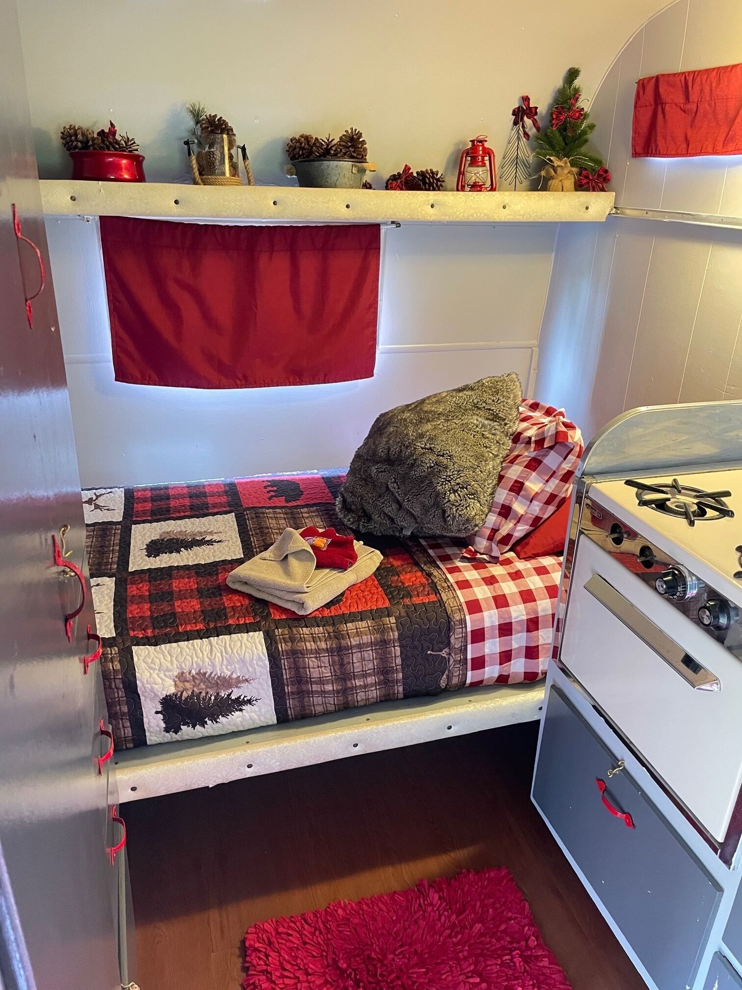 A compact bedroom with a bunk bed, a small kitchenette with a stove, and a shelf with holiday decorations.