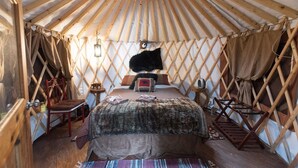 A yurt interior with a bed, a fur rug, and a wooden chair.