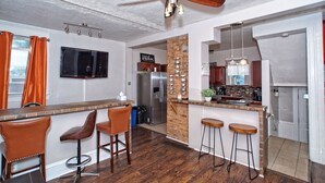 Une cuisine moderne dotée d’un îlot central, de tabourets de bar, d’un ventilateur de plafond et d’un mur d’accent en briques.