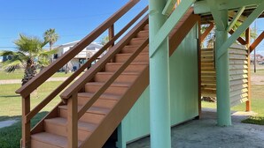 Una escalera de madera con barandilla de metal que conduce a una zona cubierta con tejado verde.