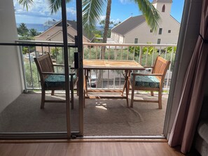 A balcony with a wooden table and chairs, a view of a church, and a palm tree.