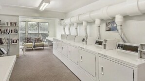 Une buanderie équipée de plusieurs machines à laver et de plusieurs sèche-linge, d’une bibliothèque et d’un coin salon avec une fenêtre.