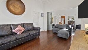 A spacious living room with a dark leather sofa, a grey sectional sofa, and a wooden coffee table.
