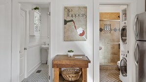 A modern bathroom with a wooden vanity, a sink, a mirror, a wall-mounted artwork, a shower, and a built-in washing machine.
