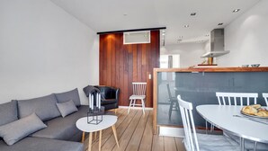 A modern living room with a grey sofa, a small round table, and a dining area with a white table and chairs.
