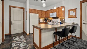 Une cuisine moderne avec des meubles en bois, un îlot central doté de tabourets, des appareils en acier inoxydable et un éclairage suspendu.
