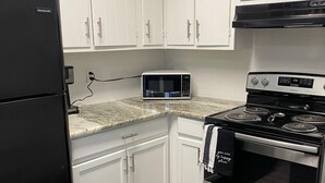 A kitchen with white cabinets, a black refrigerator, a microwave, and a stainless steel oven.