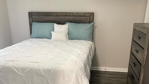 A bedroom with a wooden bed frame, white bedding, and a wooden dresser.