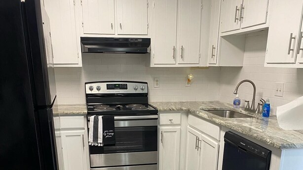 A kitchen with white cabinets, a stainless steel oven, a black dishwasher, and a granite countertop.
