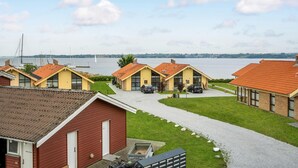 Een rij gele gebouwen met rode daken, een grindpad en een uitzicht op een meer met zeilboten.