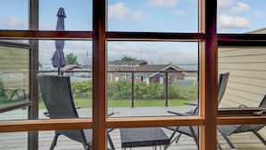 Uitzicht door een raam met houten kader, op een terras met tuinmeubilair en een huis op de achtergrond.