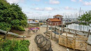 Een strandgebied met een houten constructie, een klein gebouw en een steiger met boten.